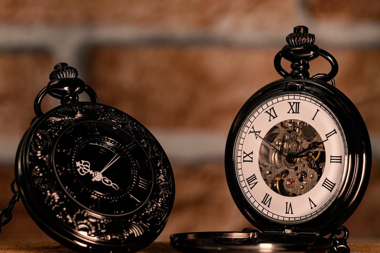 two pocket watches sitting on a table, with a brick background