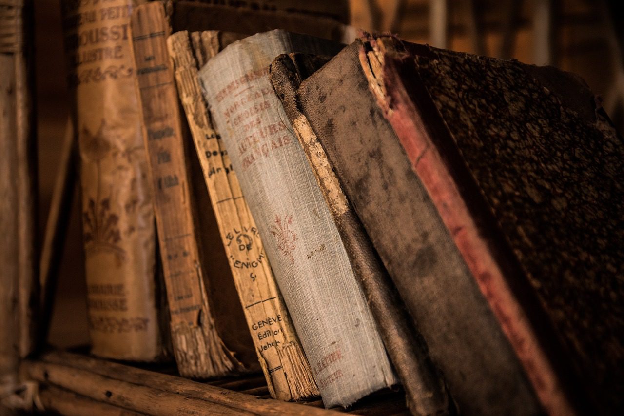 several old book on a wooden shelf, the books are leaning/sldiging down each other